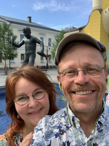 Kari ja vaimonsa hymyilevät kuvan etualalla, takana kaupunkimaisema