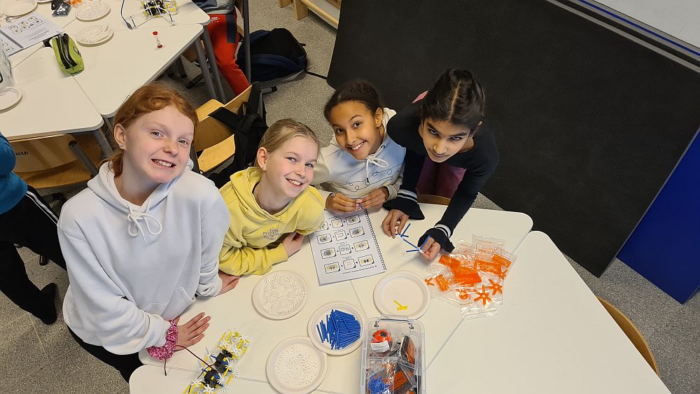 Neljä lasta hymyilee kameralle, pöydällä matematiikan havainnollistusvälineitä.