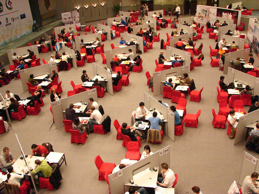 Valokuva suuresta turnauksesta, jossa kymmeniä pelipöytiä, joiden ääressä aina neljä pelaajaa.