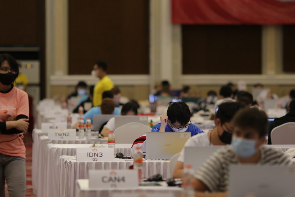 Suuressa salissa kilpailijoita tietokoneidensa ääressä
