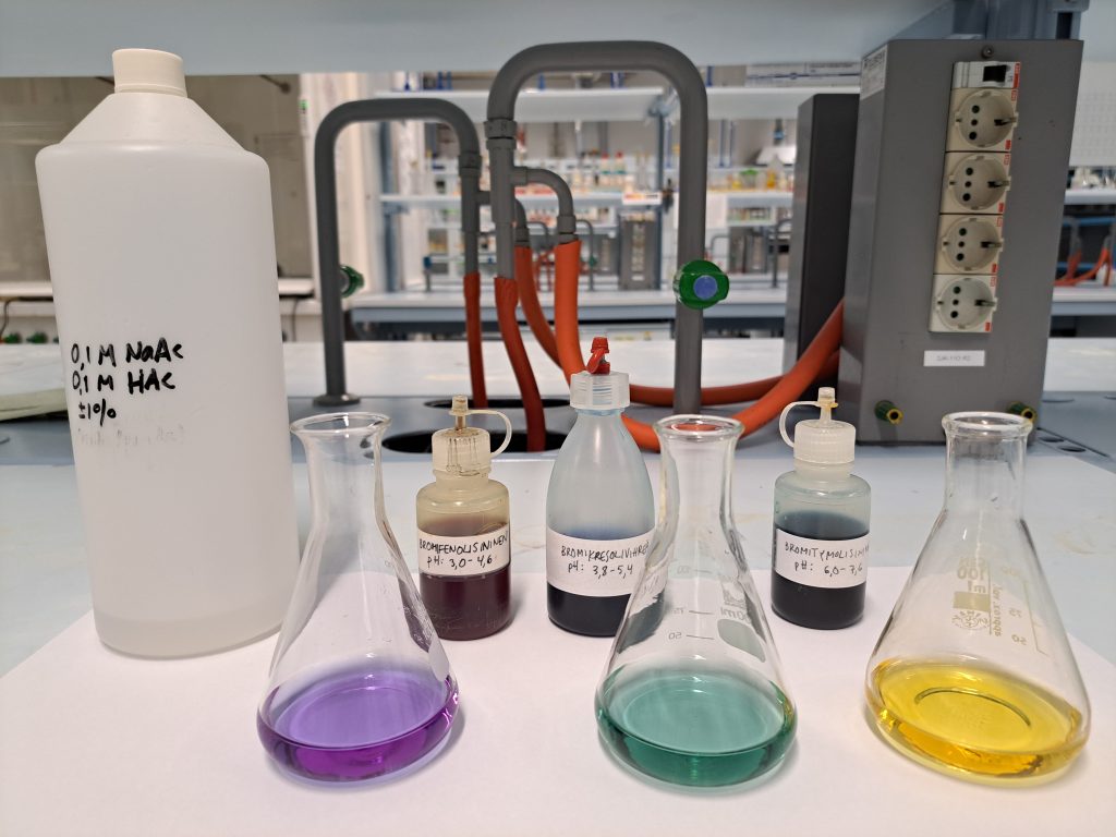 Kemian laboratoriossa kolme erlenmeyer-pulloa joissa eri väriset liuokset