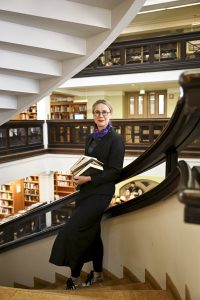 Susanna Pettersson seisoo kirjaston portaikossa syli täynnä kirjoja